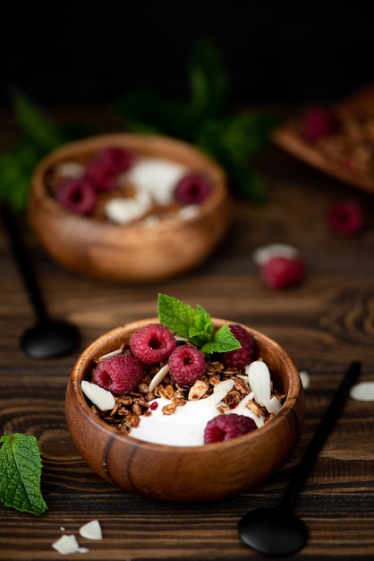 Granola with greek yogurt, mint and raspberries in wooden bowl