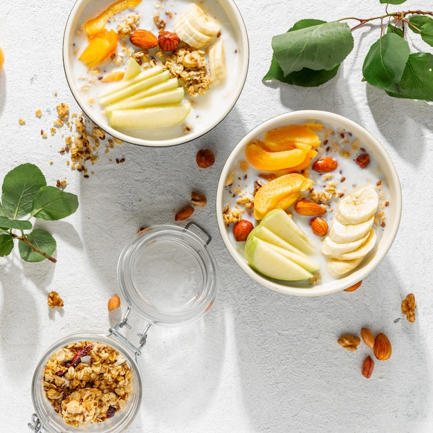 Granolagraangewas met fruit, noten, melk en pindakaas in kom op een witte achtergrond. Gezond ontbijt granen bovenaanzicht