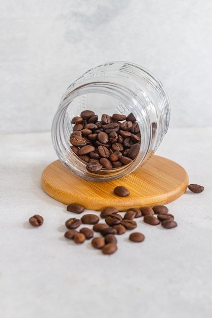 Granos de café en un vaso de cristal sobre una base de madera en fondo blanco aislado.