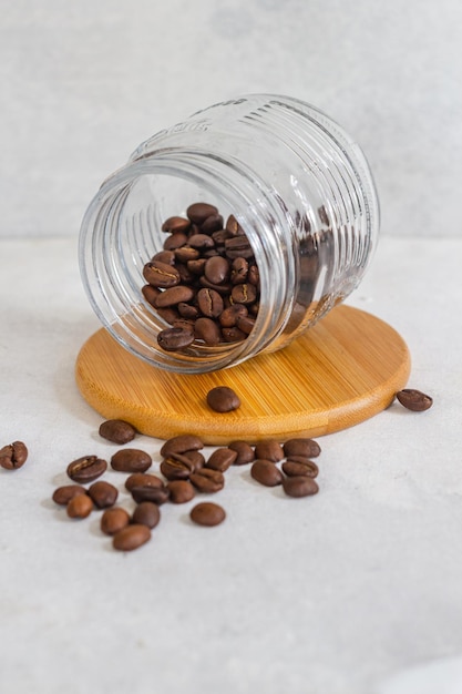 Granos de café en un vaso de cristal sobre una base de madera en fondo blanco aislado.