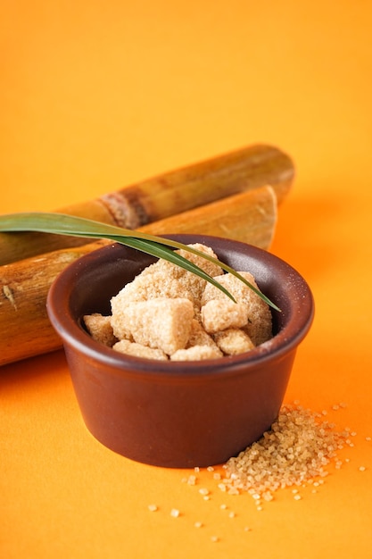 Granulated brown sugar sugarcane and green leaf on a orange background closeup Vertically