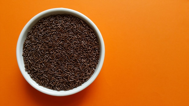 Granulated chocolate in white pot on orange table.