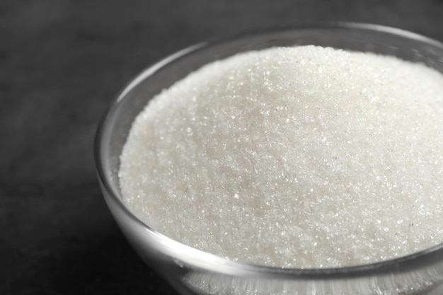 Granulated sugar in bowl on grey table closeup