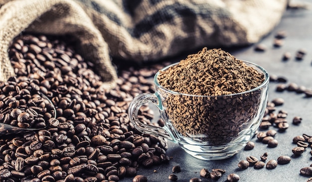 Granules of instant coffee in glass cup and coffee beans.