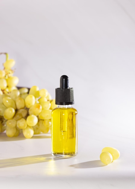 Olio di semi d'uva in una bottiglia di vetro con una pipetta e uva verde su sfondo chiaro. bio-cosmetici biologici con ingredienti vegetali.