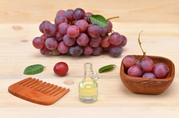 Масло виноградных косточек и розовый виноград и расческа на деревянном фоне
