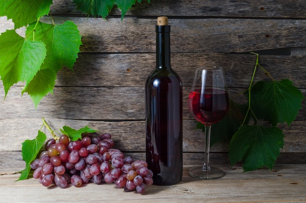 Grape Vine wijnfles en glas met wijn op een achtergrond van groen gebladerte en oude houten planken