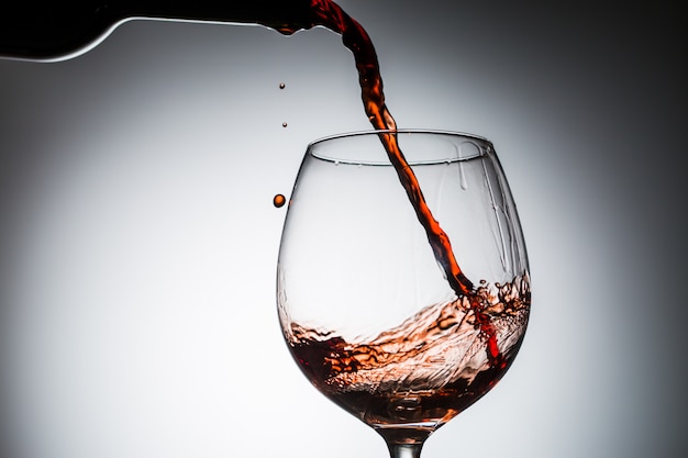 Vino d'uva versato dalla bottiglia in bicchiere da vino in vetro