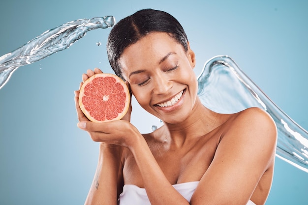 Grapefruit black woman and water for skincare cosmetics and hygiene with blue studio background Citrus young female and girl with smile body care or natural beauty to relax smooth or clear skin