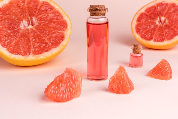 Grapefruit etherische olie in glazen flessen op roze achtergrond met vers fruit