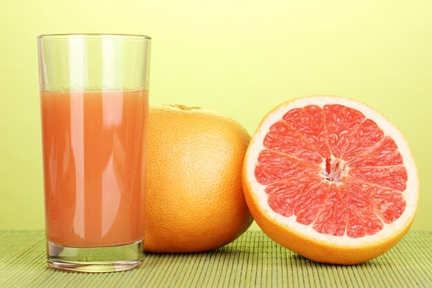 Grapefruit juice and grapefruit on bamboo mat on green background