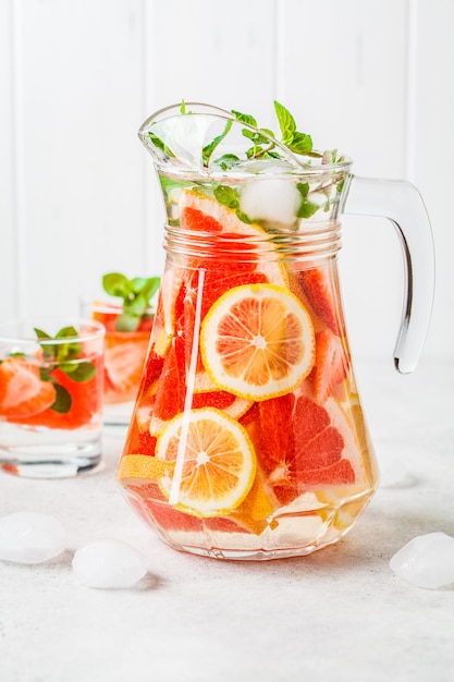 Grapefruit lemonade with lemon and mint in glass jug.