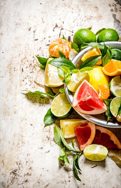 Foto pompelmo, arancia, mandarino, limone, lime in una tazza con foglie sul tavolo rustico.