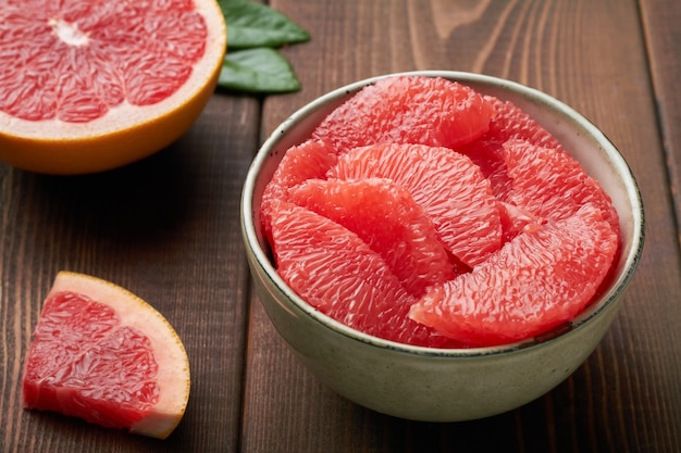 Grapefruit pieces in a bowl on brown background close up