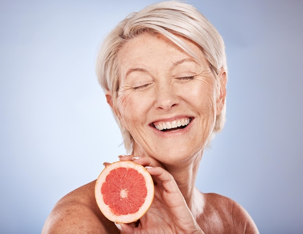 Уход за кожей с грейпфрутом и пожилая женщина в восторге от еды для здоровья кожи на фоне серого макета студии Wellness счастливая и пожилая модель с фруктами для питания, диеты и красоты