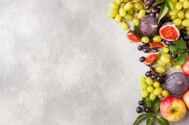 Foto uva nera e verde, fichi e foglie su un tavolo grigio