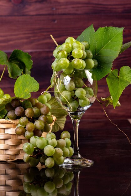 Grapes, bunches of green grapes placed together with a straw basket on reflective surface, selective focus.