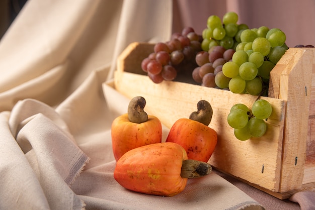 Grapes in a wooden box and cashews with fabrics in the background, low depth of field