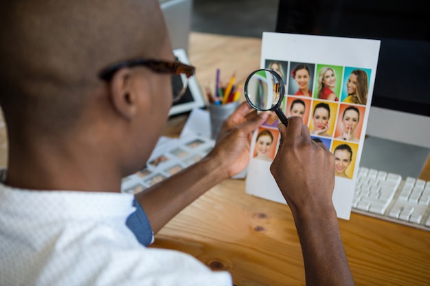 Graphic designer looking at photograph with magnifying glass at desk