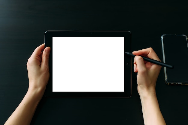 Graphic designer's hands working on tablet with digital pen, close up. Empty white screen, black table.