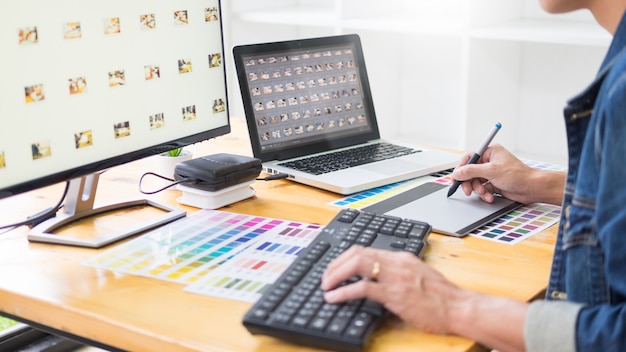 Graphic designer team working on web design using color swatches editing artwork using tablet and a stylus At Desks In Busy Creative Office.