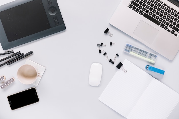 Graphic digital tablet and laptop mock up with office objects on white table