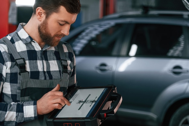 Foto le informazioni grafiche sono sul tablet l'uomo in uniforme sta lavorando nel salone dell'auto