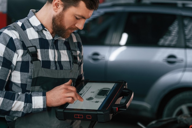 Foto le informazioni grafiche sono sul tablet l'uomo in uniforme sta lavorando nel salone dell'auto