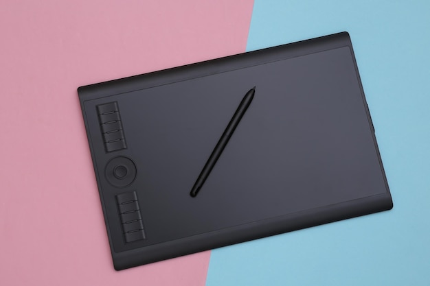 Graphic tablet with pen on pink blue background. Top view