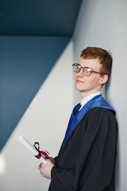 Ritratto verticale grafico di un giovane che indossa abito da laurea e tiene in mano un diploma mentre sorride alla telecamera al college