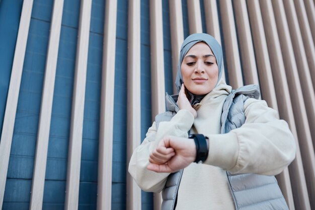 Graphic waist up portrait of modern Middle-Eastern woman checking smartwatch during morning run, copy space