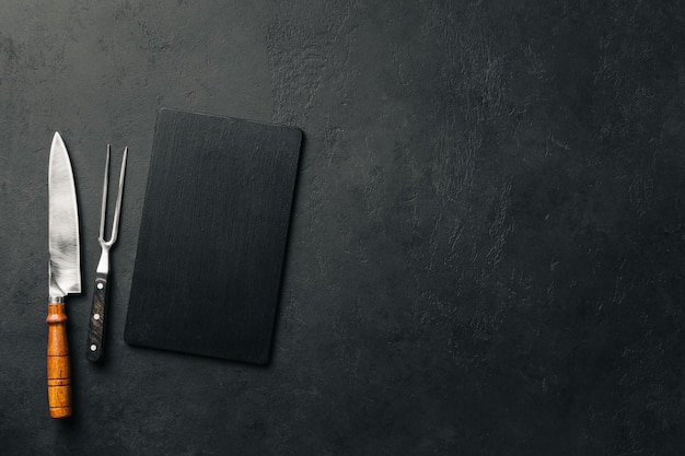 Graphite plate with knife and meat fork over black concrete background