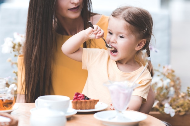 Grappig babymeisje dat aardbeientaart eet terwijl ze met moeder in café zit