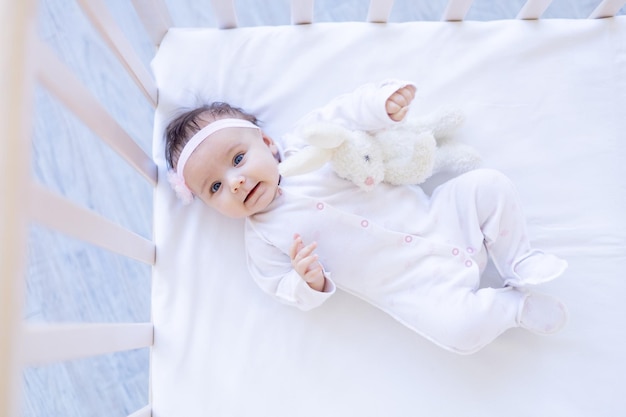 Grappig babymeisje met rode harten op een bed op een wit katoenen bed dat valentijnsdagconcept glimlacht of lacht