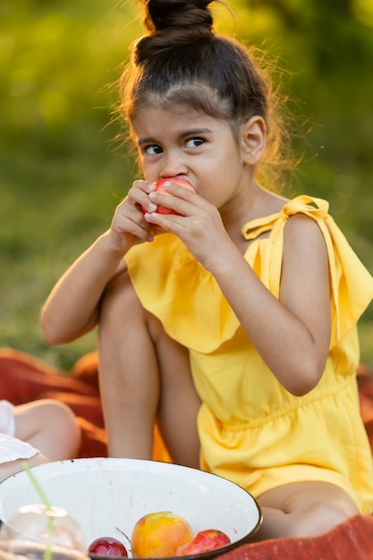 Grappig donker meisje eet een appel in de tuin Kind eet buiten fruit GGO-vrij voedsel