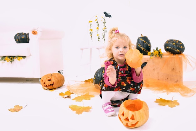 Grappig en schattig klein blond curvemeisje met pompoen in Halloween-decoratie