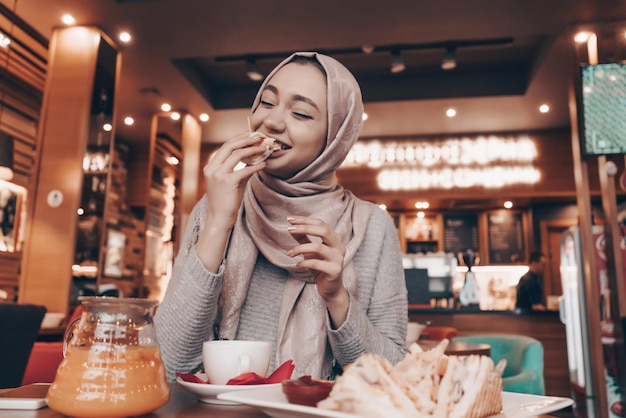 Grappig jong Arabisch meisje in hijab in een gezellig restaurant, heerlijk eten