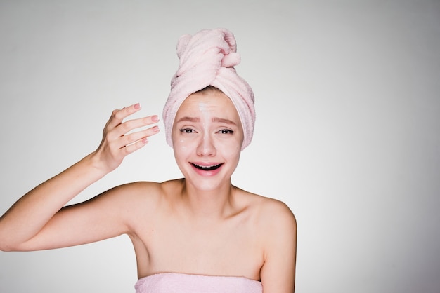 Grappig jong meisje met een roze handdoek op haar hoofd brengt vochtinbrengende crème op het gezicht aan