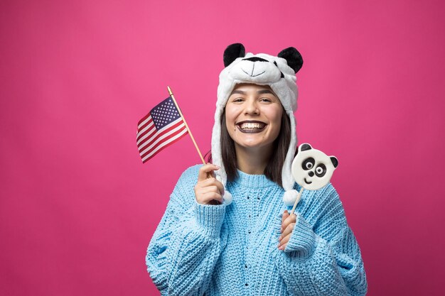 Grappig jong meisje met lekkere pandalollipop in haar hand en een hoed op zijn hoofd op een roze achtergrond