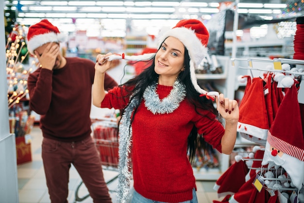 Grappig jong stel dat kerstmiskleren in supermarkt, familietraditie probeert. winkelen in december van vakantiegoederen en decoraties