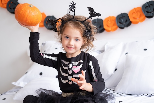 Grappig kaukasisch kindmeisje in heksenkostuum dat plezier heeft in versierd voor halloween-slaapkamer