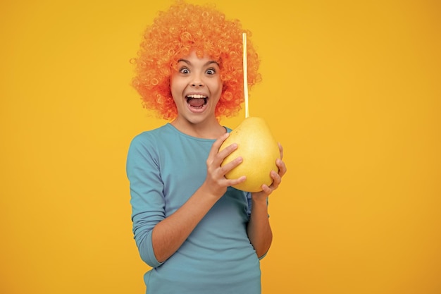 Foto grappig kind meisje in pruik houdt grote citrusvruchten pummelo of pomelo vol vitamine gezonde kinderen eten opgewonden tiener blij verbaasd en dolblij emoties