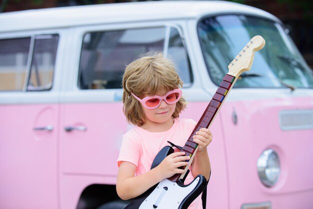 Grappig kind met blond krullend haar dat gitaar speelt op roze achtergrond Muziekschool voor kinderen