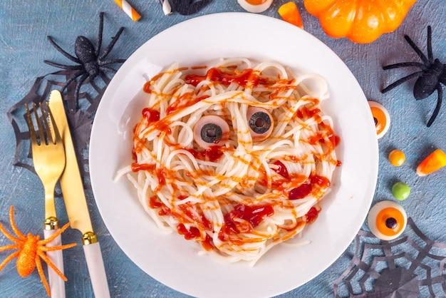 Grappig kindervoedsel voor Halloween lunch of diner Spaghetti pasta met worst creatief recept in de vorm van mummies met ketchup gemaakt bloed met Halloween decor op blauwe betonnen tafel kopieerruimte