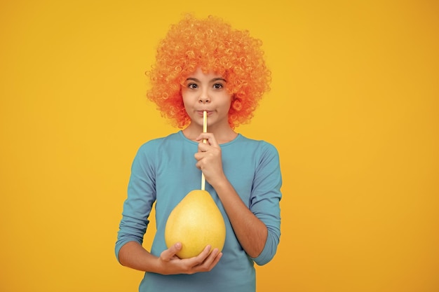 Grappig kindmeisje met pruik houdt grote citrusvruchten pummelo of pomelo vol vitamine gezonde kinderen aan het eten