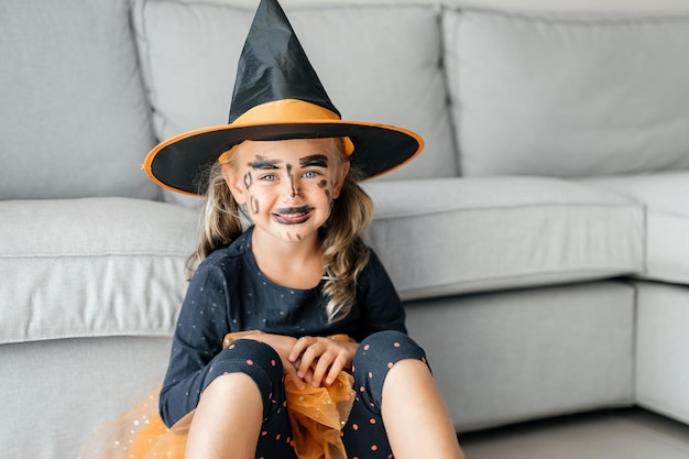 Grappig klein meisje met heksenhoedkostuum en make-up Gelukkig kind in halloweenkostuum klaar voor Halloween-feest