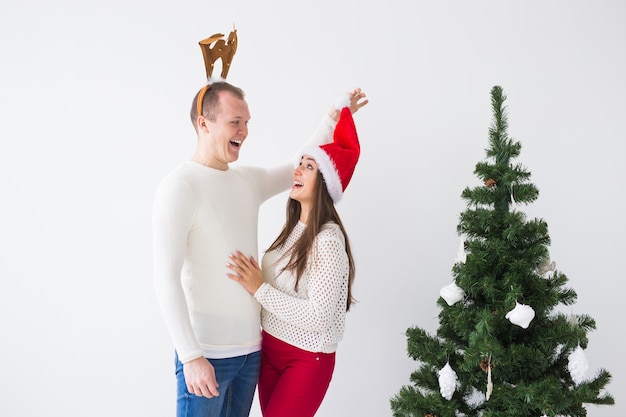 Grappig liefdevol paar in de buurt van de kerstboom. Man draagt herten hoorns en vrouw draagt kerstmuts