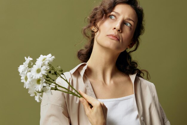 Grappig liefelijk overstuur krullend mooi vrouwtje in linnen casual shirt houdt kamille bloemen opzij kijkt omhoog poseren geïsoleerd op over olijfgroen pastel achtergrond de natuur is schoonheid concept kopieer ruimte