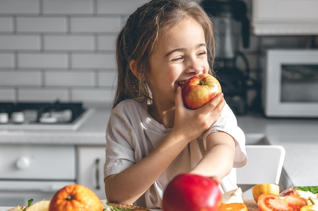 Grappig meisje dat appels eet in het keukengezondheids- en voedingsconcept