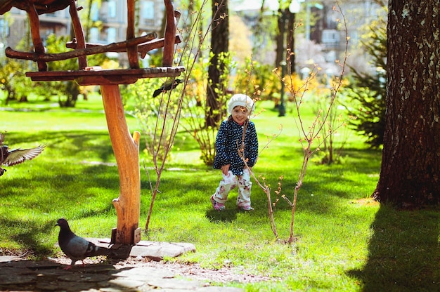 grappig meisje dat in het groene park speelt, rent en duiven achtervolgt. zonnige lentedag. Familie
